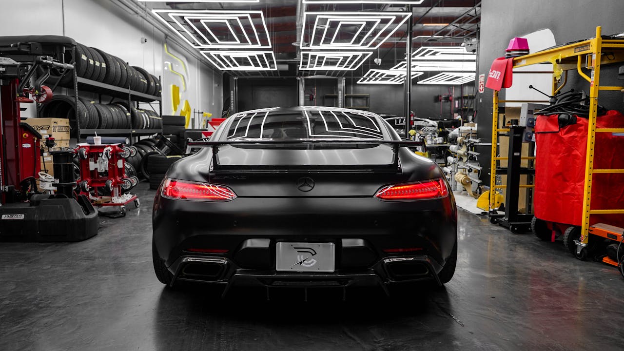 Rear view of a black Mercedes-Benz in a high-end auto workshop with modern lighting and equipment.